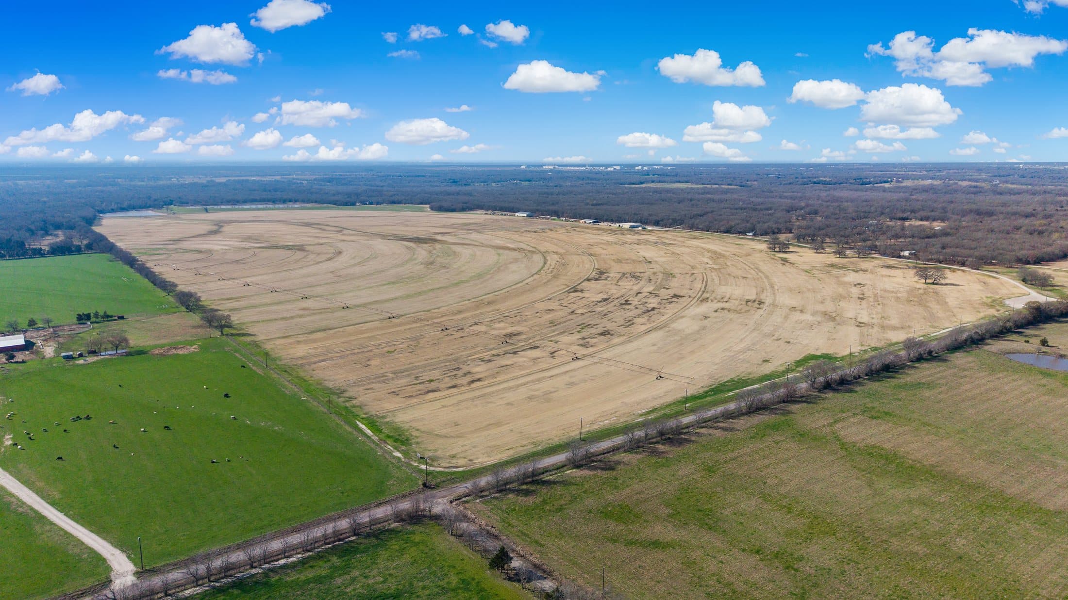 High aerial overview of the primary site looking across cultivated acreage and tree line