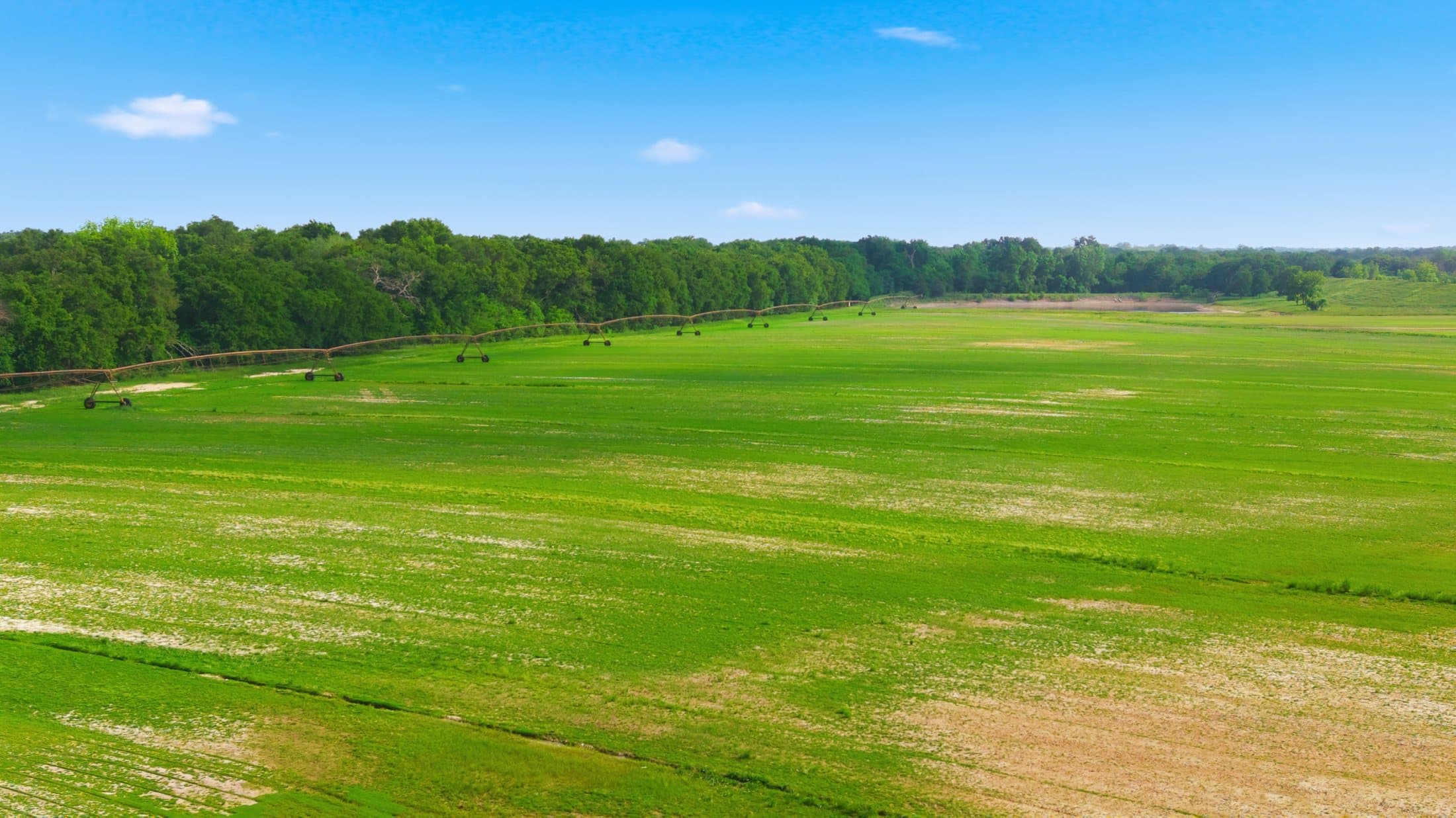 Summer aerial of an irrigation pivot extending across a green production field