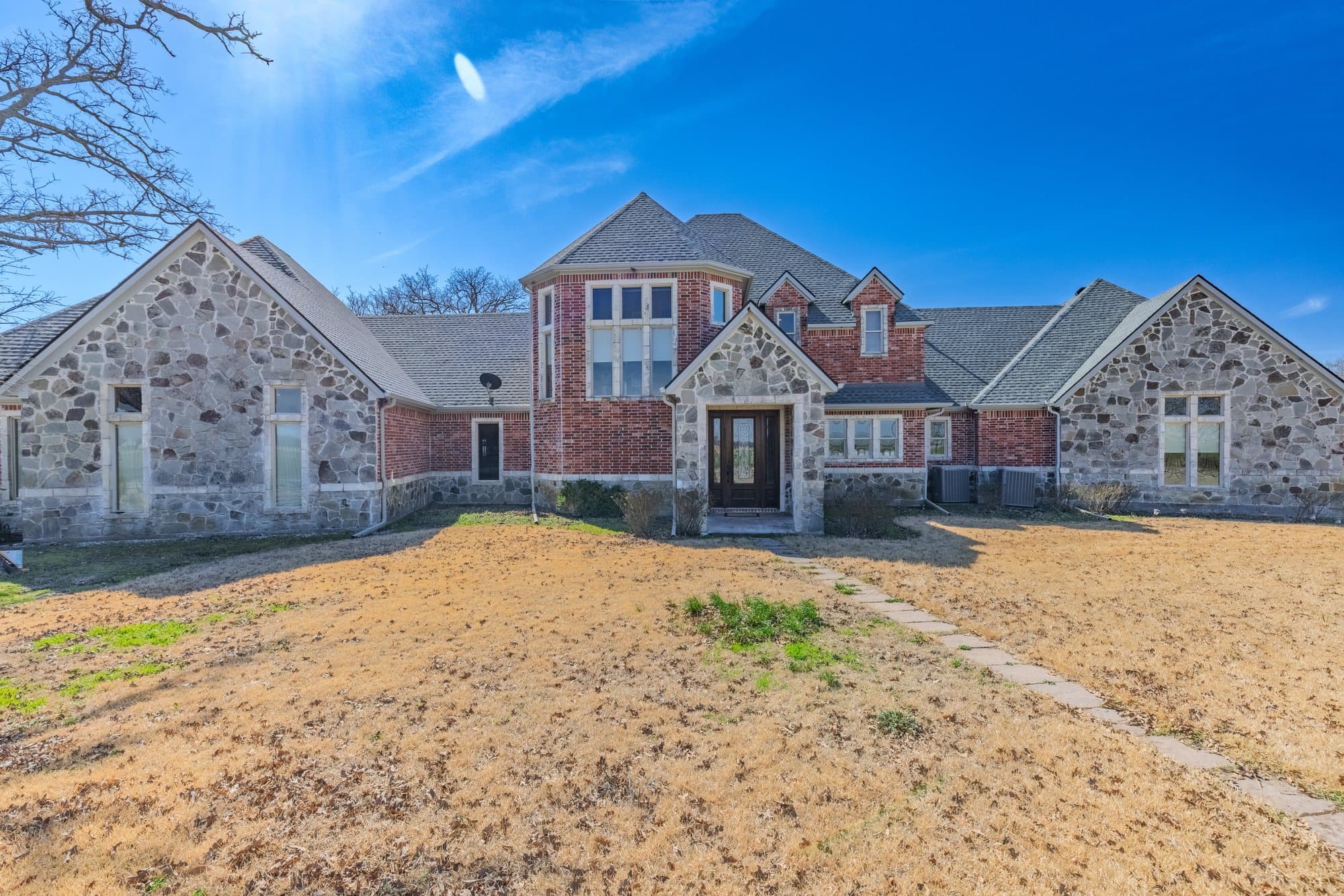 Front exterior of the main residence at 752 CR 3103 — red brick and grey stone home with bright sky